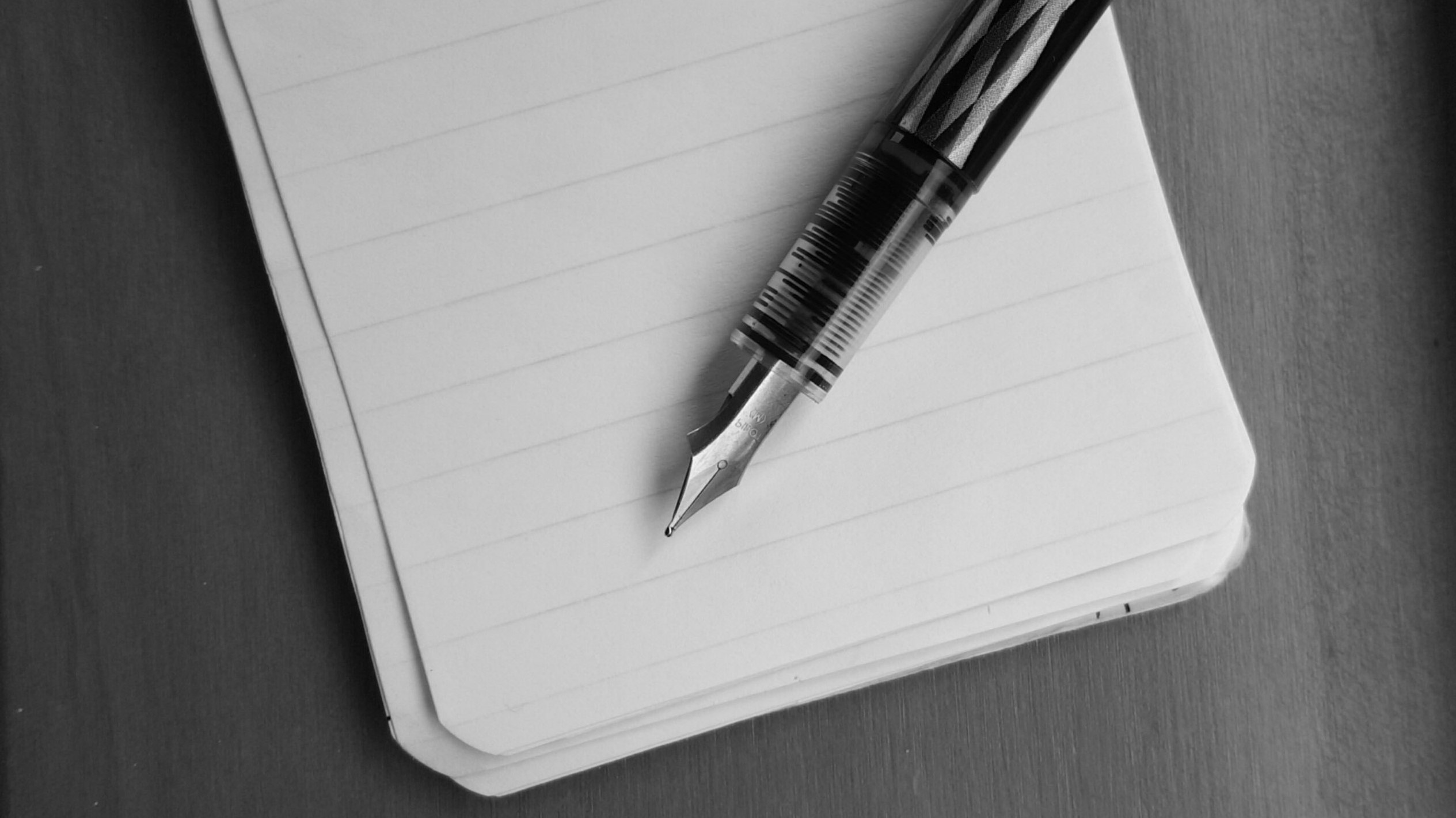 black and white close up of an ink pen lying across a small notepad
